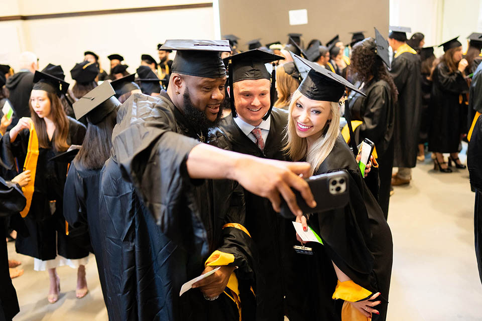 three graduates in regalia pose for a selfie