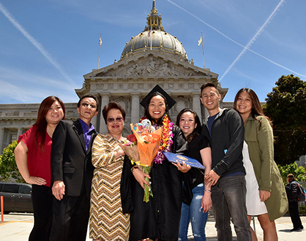 Graduate and family members pose for a photo in front of SF City Hall