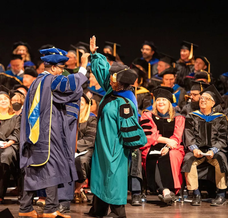 Dean Blake shares a high five with a PhD grad