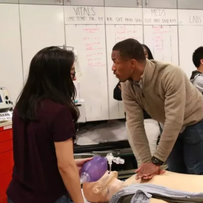 school of medicine post-baccalaureate student training for CPR on a dummy as an instructor watches