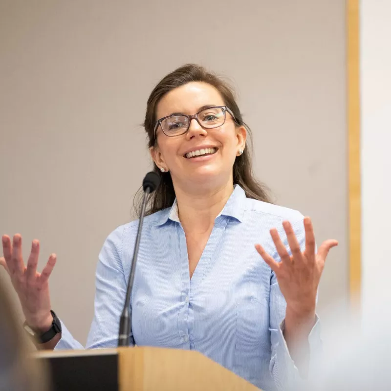 a speaker at a podium smiling, and gesturing with both hands
