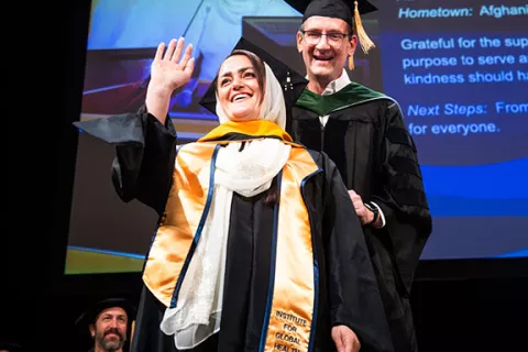 a grad waves to family as she is hooded on stage