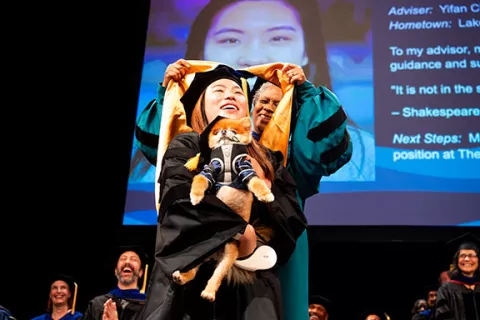 a student is hooded while holding a small dog