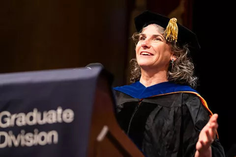 Michelle Arkin speaks at podium in regalia