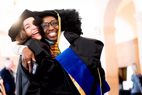 two students in academic regalia share a hug