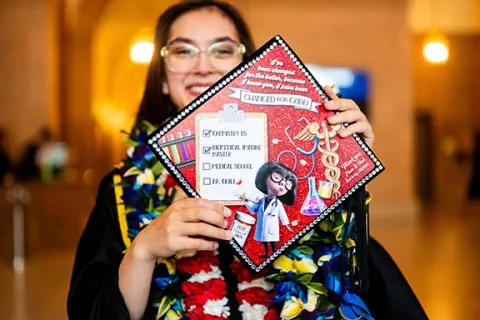 a grad in regalia shows off her decorated mortarboard cap