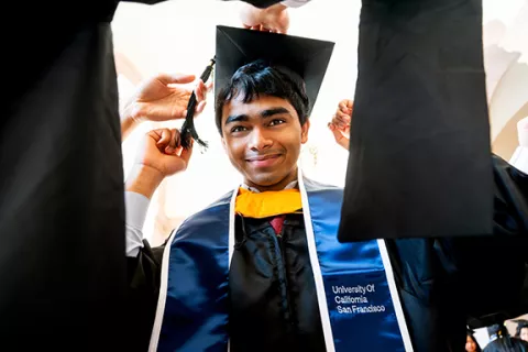 a grad adjusts his mortarboard cap with help from friends