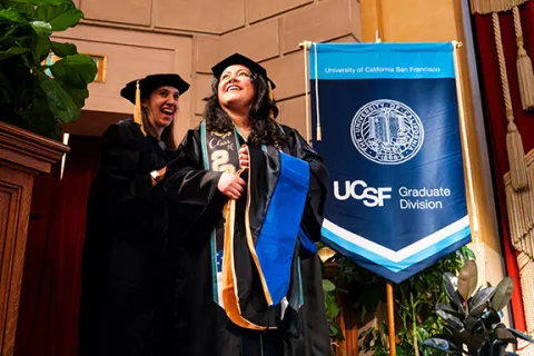 two grads wait at edge of stage to be hooded