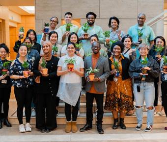 a group of smiling people poses for a photo holding plants in pots that they have decorated in a workshop