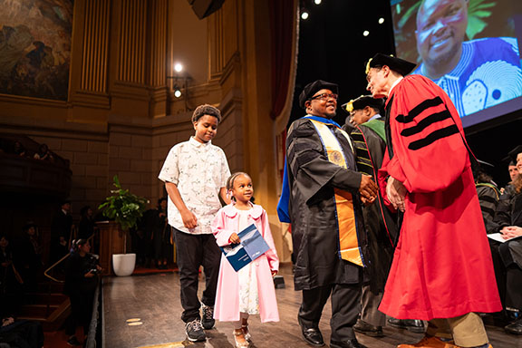 A PhD grad is joined by his children at commencement ceremony