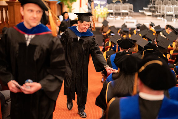 a faculty member greets a grad during commencement recessional