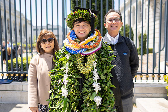 A grad with voluminous commencement regalia poses with family members