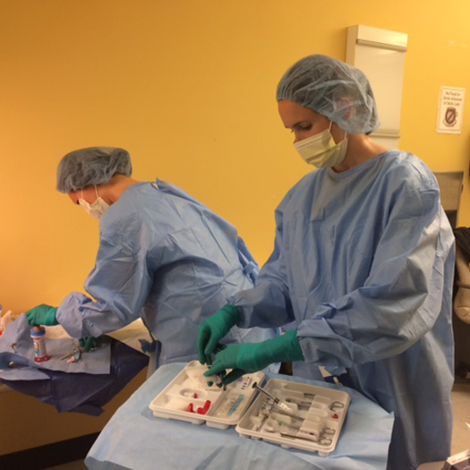 two people in hospital scrubs and headcoverings working in a clinical setting
