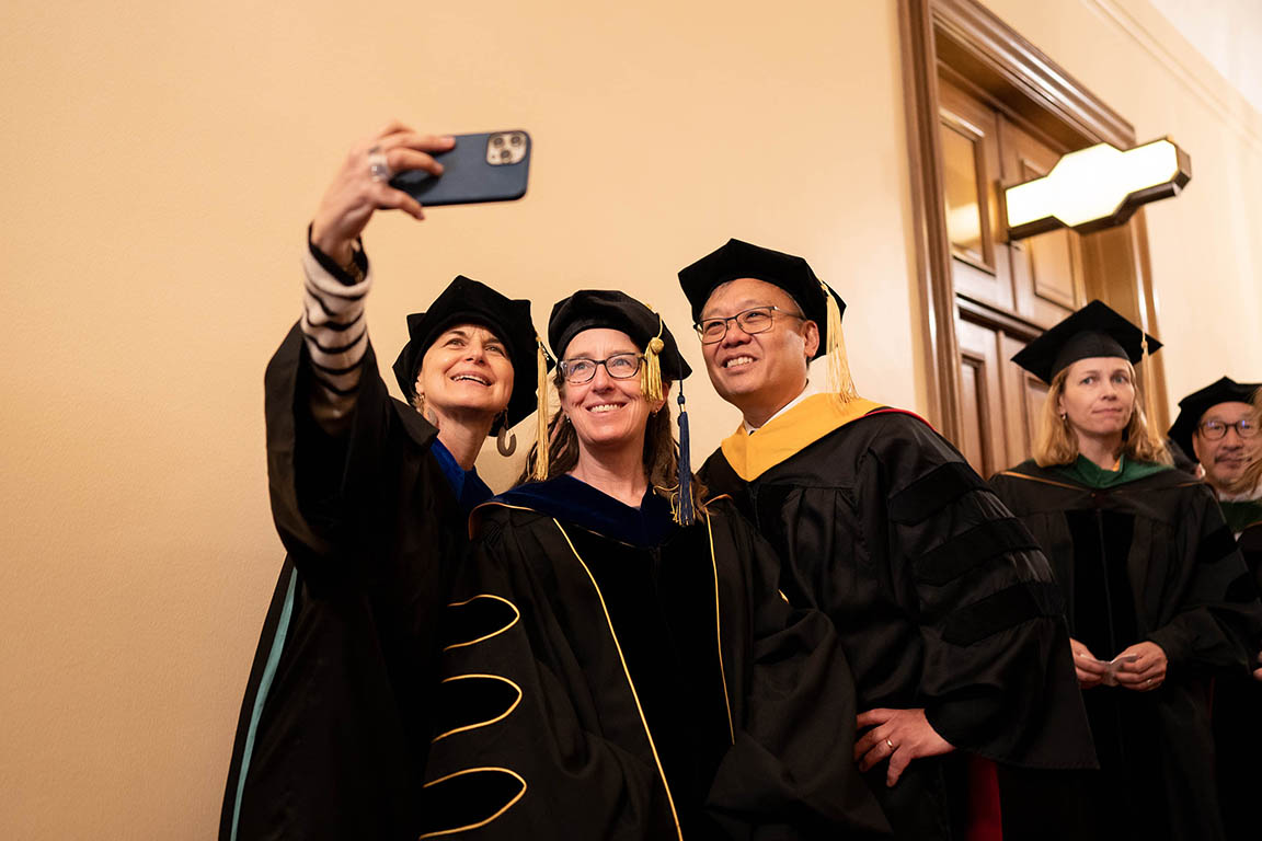 three faculty members in academic regalia take a selfie