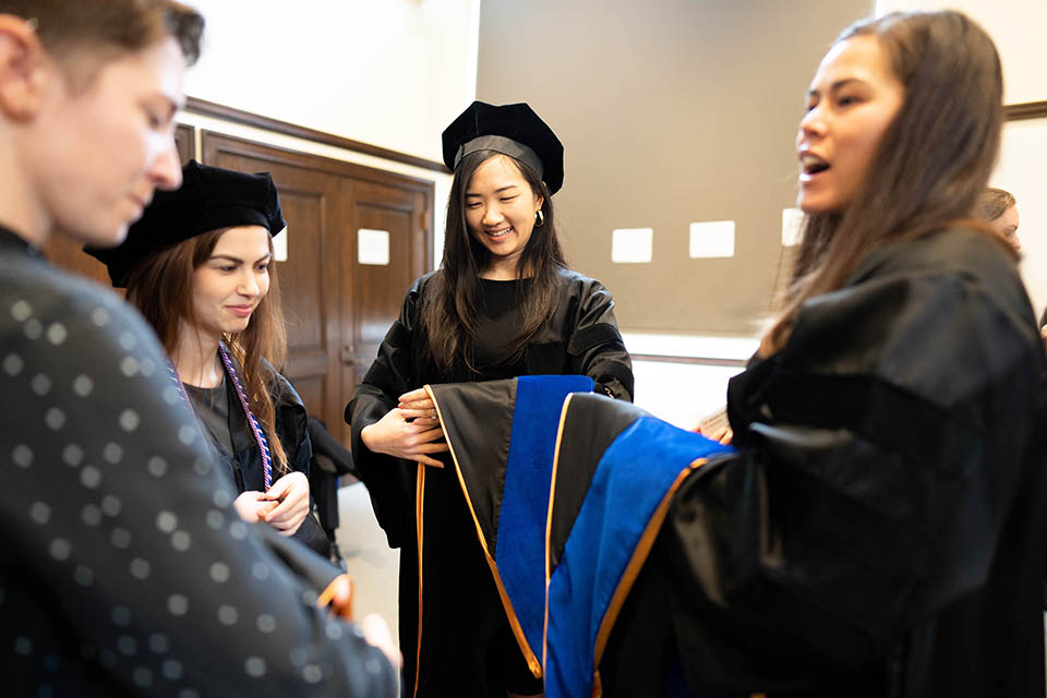 graduates practice how to hold academic hoods before the ceremony
