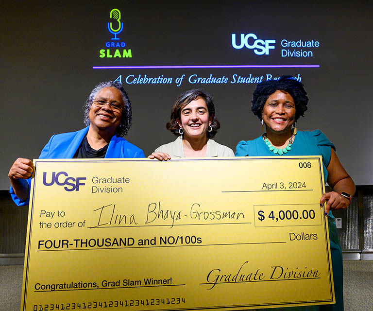 Ilina Bhaya-Grossman, Grad Slam 2024 1st prize winner, holds a giant check, flanked by Graduate Dean Nicquet Blake and Assistant Dean D'Anne Duncan