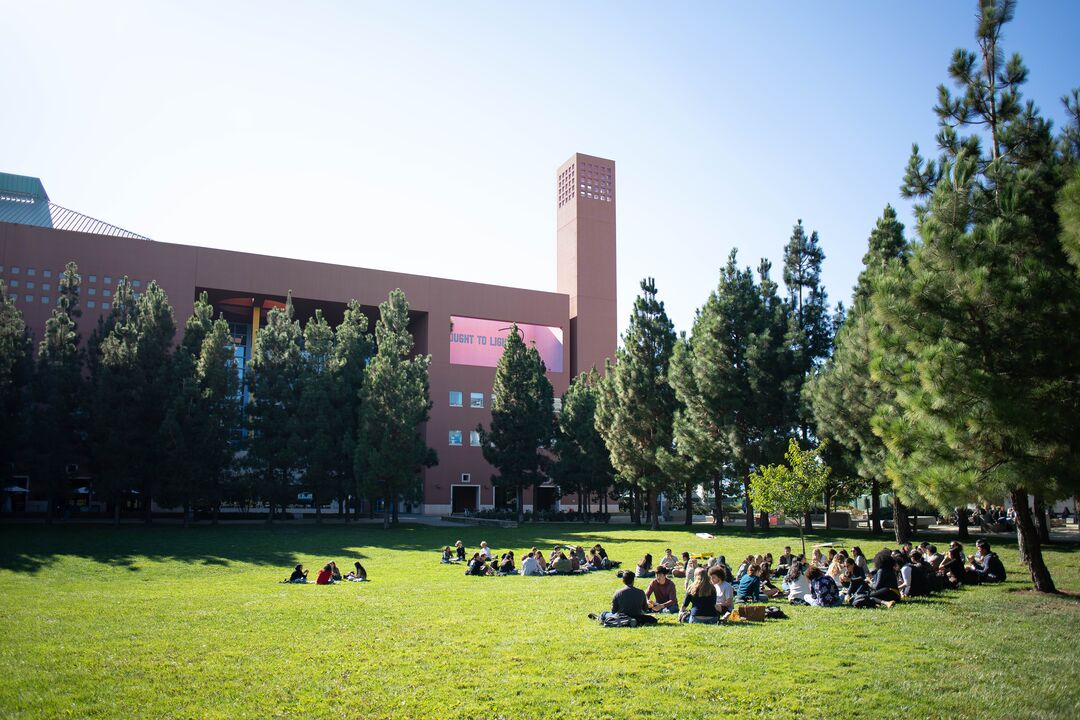 students sit on sunny Koret Quad with Rutter Center in the background