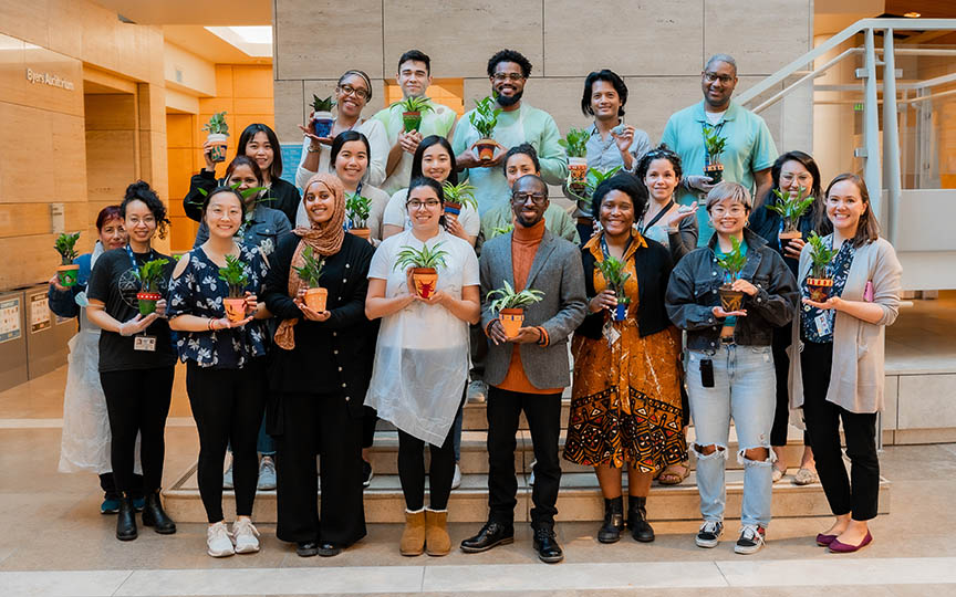 Participants in plant art workshop gather for a group photo holding there plants in painted pots.