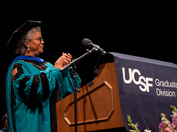 Nicquet Blake, PhD, attired in academic regalia, applauds the graduates from the podium