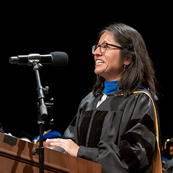Mercedes Paredes, MD, PhD, dressed in academic regalia, speaks at a podium