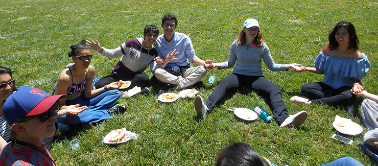 several students sit in the grass enjoying a picnic